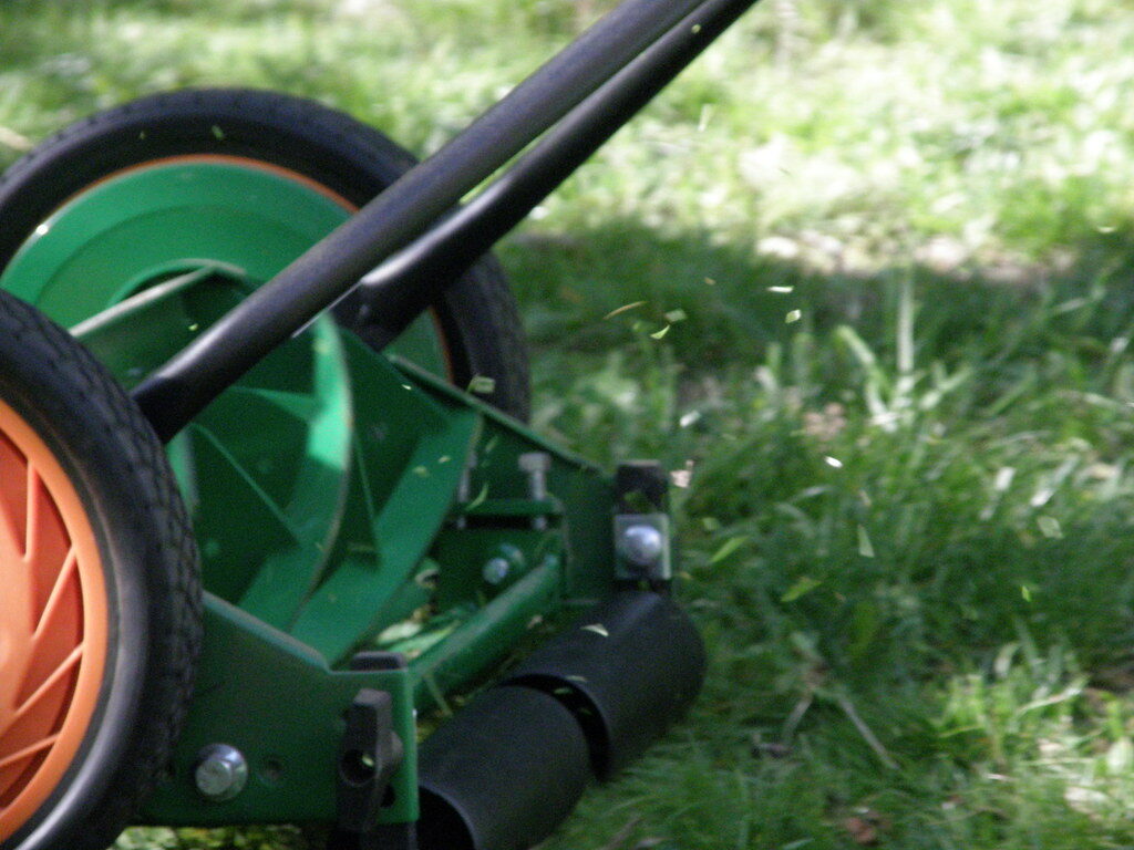 Close-up of a mower blade cutting grass with clippings flying
